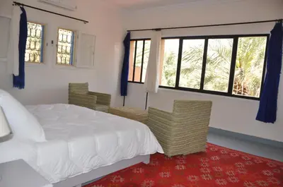 a bedroom with a bed and chairs and windows at Maison La Berberina in Goulmima