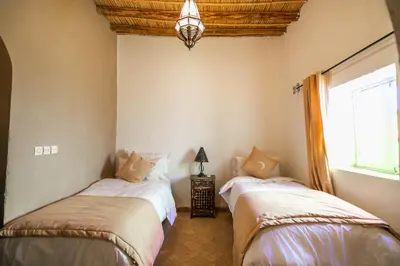 a bedroom with two beds and a window at Riad Kasbah Aiour in Merzouga