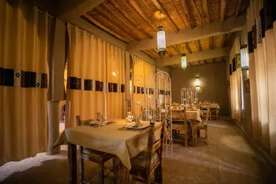 a dining room with tables and chairs and curtains at Riad Kasbah Aiour in Merzouga