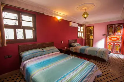 two beds in a room with red walls and windows at Dar El Mathaf FES in Fès