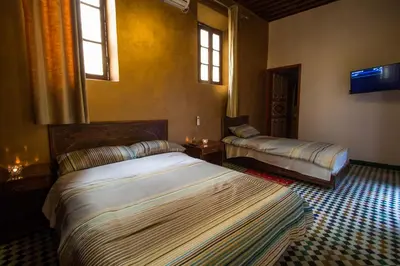 a bedroom with two beds and a tv and windows at Dar El Mathaf FES in Fès