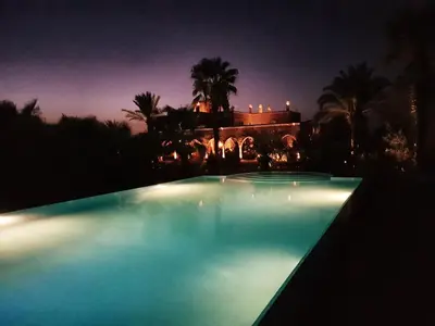 a swimming pool at night with a house in the background at Ksar Salha in Marrakech