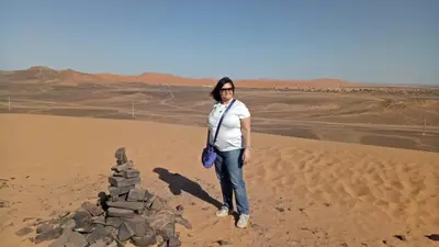 a woman standing next to a pile of rocks in the desert at Night Desert Camp in Merzouga