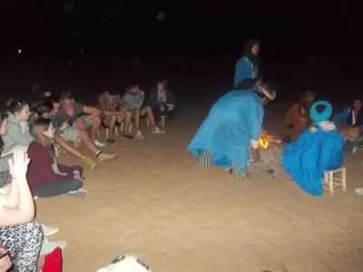 a group of people sitting around a fire on the beach at Bivouac Draa in Zagora