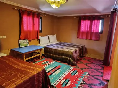a room with two beds and a table and red curtains at Bivouac Lot Of Stars in Ouarzazate