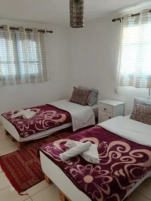 a bedroom with two beds and two tables and windows at Relais De Tahla in Ain Boumahdi