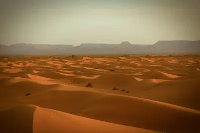 a desert with sand dunes and mountains in the background at Dar Azawad Royal Desert Camp - Erg Chigaga Luxury Glamping in Mhamid
