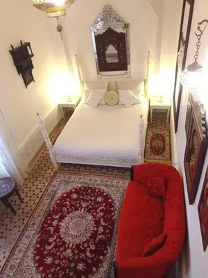 a bedroom with a white bed and a red couch at Riad Dar Arsama in Fès