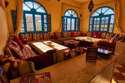 a restaurant with couches and tables and windows at Maison D'hotes Sahara in Aoufous