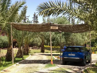 a blue truck parked under a bamboo structure with palm trees at Teacook Marrakech in Ouled el guerne