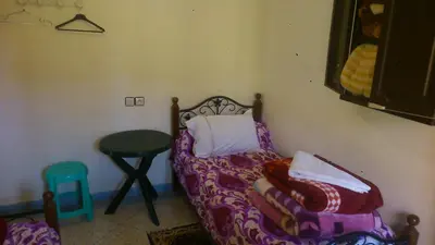 a bedroom with a bed and a table and a stool at Hotel Imilchil in Zaouiat Cheikh