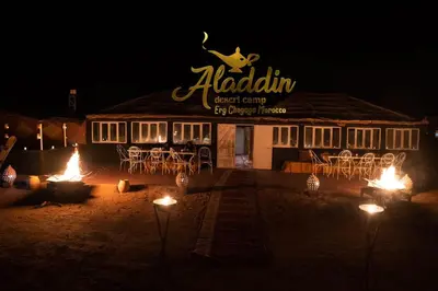 a restaurant at night with fires in front of it at Aladdin Desert Camp - Mhamid Erg Chigaga Escape in El Gouera