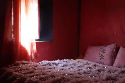a bed in a red room with a window at Hike and Chill Homestay in Tinerhir