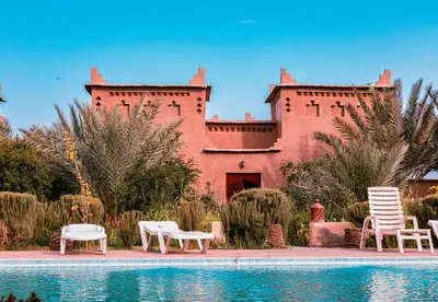 a building with chairs and a pool in front of it at Maison D'hôte Amridil in Skoura