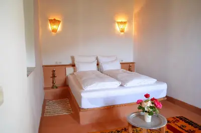 a bedroom with a bed with white sheets and a table at Le Douar Berbere in Ourika