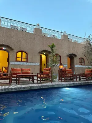 a swimming pool with wooden benches and a building at La Petite Kasbah in Zagora