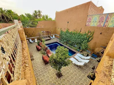 an outdoor patio with a pool and chairs and trees at La Petite Kasbah in Zagora