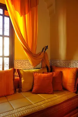 a couch with orange pillows in a room with a window at Riad Ibn Battouta & Spa in Fès