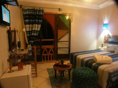 a bedroom with two beds and a table and a chair at Fibule Du Draa Kasbah D'hôtes in Zagora
