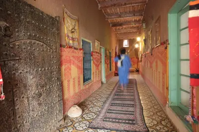 a person walking down a hallway in a building with a mosaic floor at Fibule Du Draa Kasbah D'hôtes in Zagora