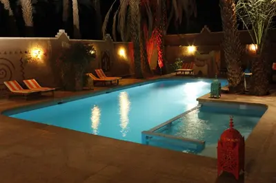 a swimming pool at night with chairs and lights at Fibule Du Draa Kasbah D'hôtes in Zagora