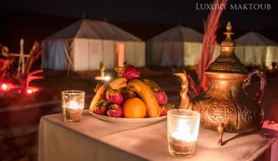 a bowl of fruit on a table with a tea pot and candles at Luxury Maktoub in Merzouga