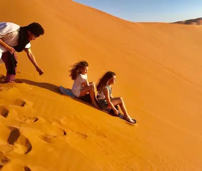 a man and two girls sitting on a sand dune at Luxury Maktoub in Merzouga