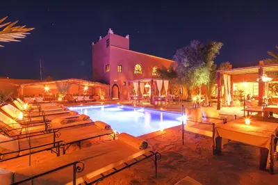 a pool with benches and a building at night at Hotel Kasbah Sahara Services - M'Hamid El Ghizlane in Mhamid