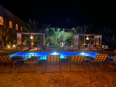 a group of chairs and tables in front of a pool at night at Hotel Kasbah Sahara Services - M'Hamid El Ghizlane in Mhamid