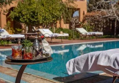 a table with glasses and a bottle next to a pool at Bassatine Skoura in Skoura
