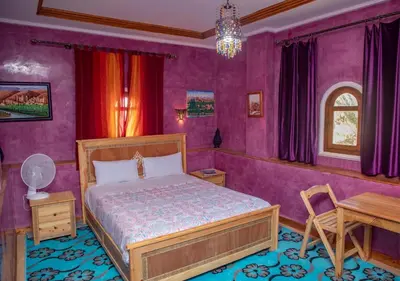a bedroom with purple walls and a bed and a table at Bassatine Skoura in Skoura