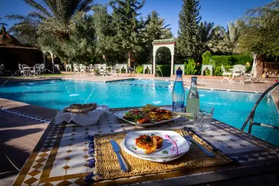 a table with a plate of food next to a swimming pool at Paradis Touareg in Zagora