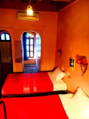 a bedroom with two beds with red sheets and a window at Kasbah Tiriguioute in Skoura