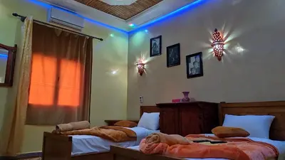 two beds in a bedroom with blue lights on the wall at Dar Calme Chez El Bouhali in Skoura