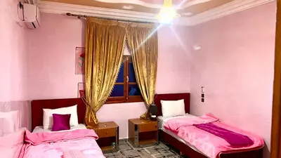two beds in a room with pink walls and a window at Dar Calme Chez El Bouhali in Skoura
