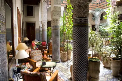 a lobby with columns and chairs and tables and plants at Riad Al Bartal in Fès