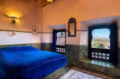 a bedroom with a blue bed and two windows at Hôtel Riad Dar Daïf in Ouarzazate