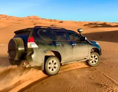 a blue jeep driving in the desert at Camp Sahara Holidays in Mhamid