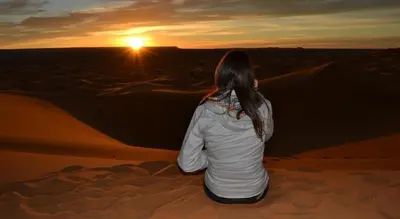 a woman sitting in the desert watching the sunset at Camp Sahara Holidays in Mhamid
