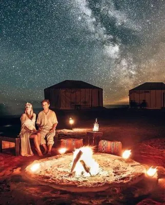 a man and a woman sitting next to a fire at Camp Sahara Holidays in Mhamid