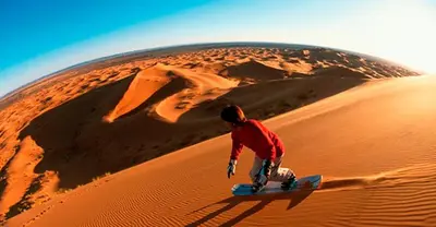a man riding a snowboard down a sand dune at Camp Sahara Holidays in Mhamid