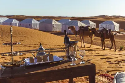 a table in the middle of the desert with camels at DWO Golden Camp Merzouga in Merzouga