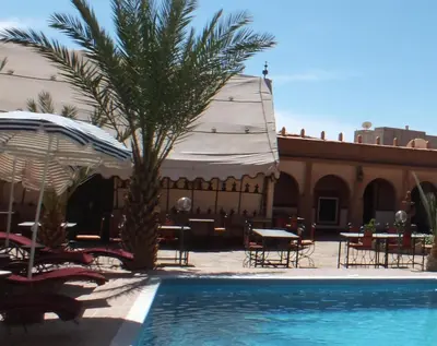 a palm tree next to a swimming pool with a tent at Hotel Tomboctou in Tinerhir