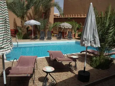 a swimming pool with chairs and umbrellas next to at Hotel Tomboctou in Tinerhir