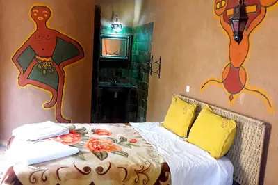 a bedroom with a bed with paintings on the walls at Hamada Du Draa in Mhamid