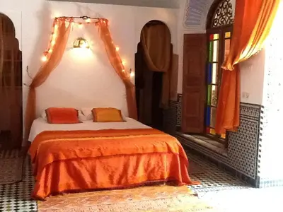 a bedroom with a bed with orange sheets and a window at Riad Tayba in Fès