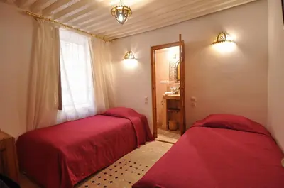 two beds in a room with red sheets and a window at Riad Tayba in Fès