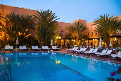 a large swimming pool with white chairs and a building at Berbère Palace in Ouarzazate