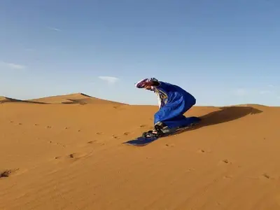 a person riding a snowboard on a sand dune at M'hamid Desert Camp Tours in Mhamid