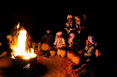 a group of people sitting around a large fire at M'hamid Desert Camp Tours in Mhamid